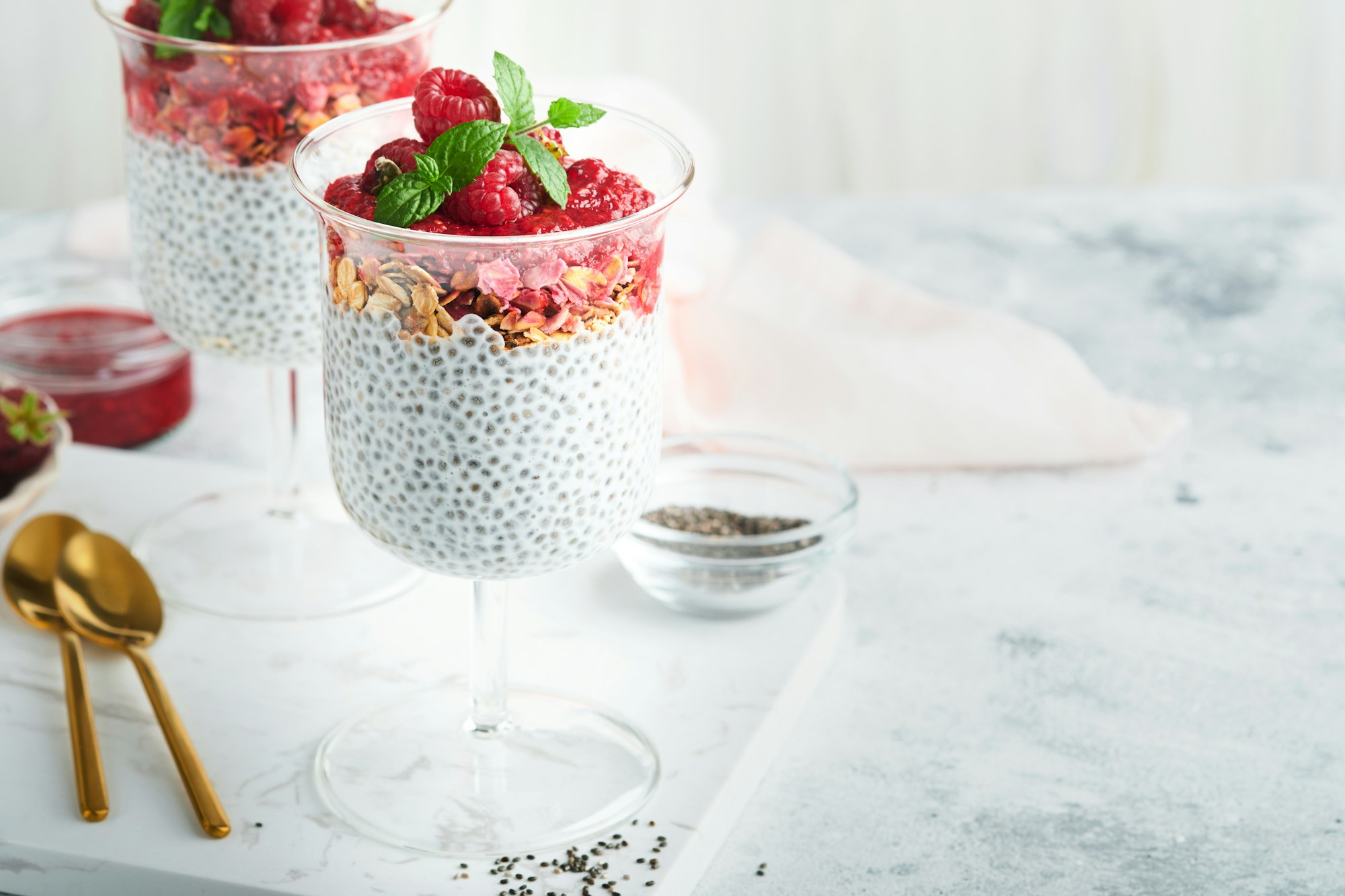 Chia pudding. Healthy vanilla chia pudding in glass with fresh raspberries and mint on white backgro