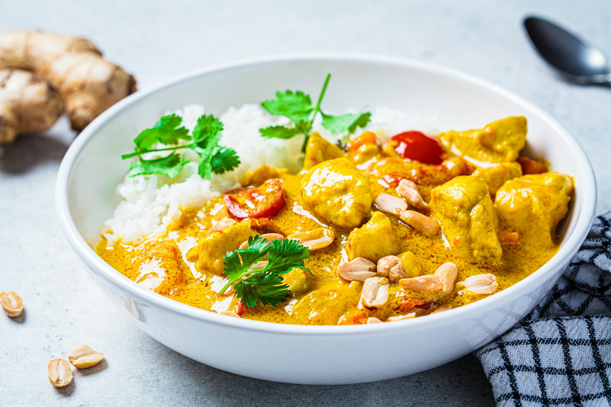 Thai chicken and peanut curry with rice in white bowl, gray background. Asian cuisine concept.